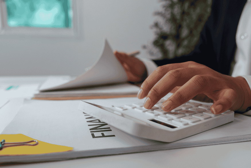Mensch macht finanziellen Jahrescheck mit Taschenrechner und Finanzunterlagen am Schreibtisch